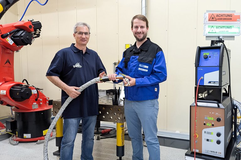 Ein Mann von der SUT und ein Mann von der SLV Halle GmbH halten ein Laserhandschweißgerät in den Händen