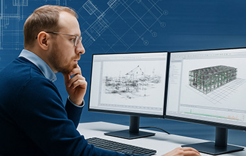 Mann mit Brille und dunkelblauem Pullover arbeitet konzentriert an zwei Monitoren mit technischen 3D-Konstruktionszeichnungen.