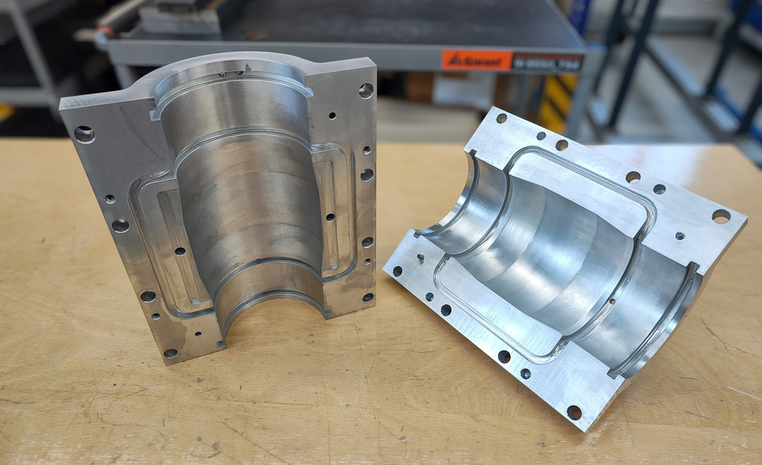 Zweiteiliges metallisches Formwerkzeug mit präzise bearbeiteten Hohlräumen liegt geöffnet auf einem Holztisch in einer Werkstattumgebung