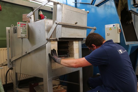 Mitarbeiter öffnet die Tür eines Ofens, um Betonstahlproben thermisch altern zu lassen.