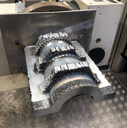 Metallischer Werkstückaufbau mit schichtweise aufgetragenen Schweißraupen auf einem Maschinenbett, industrieller Hintergrund mit Riffelblechboden